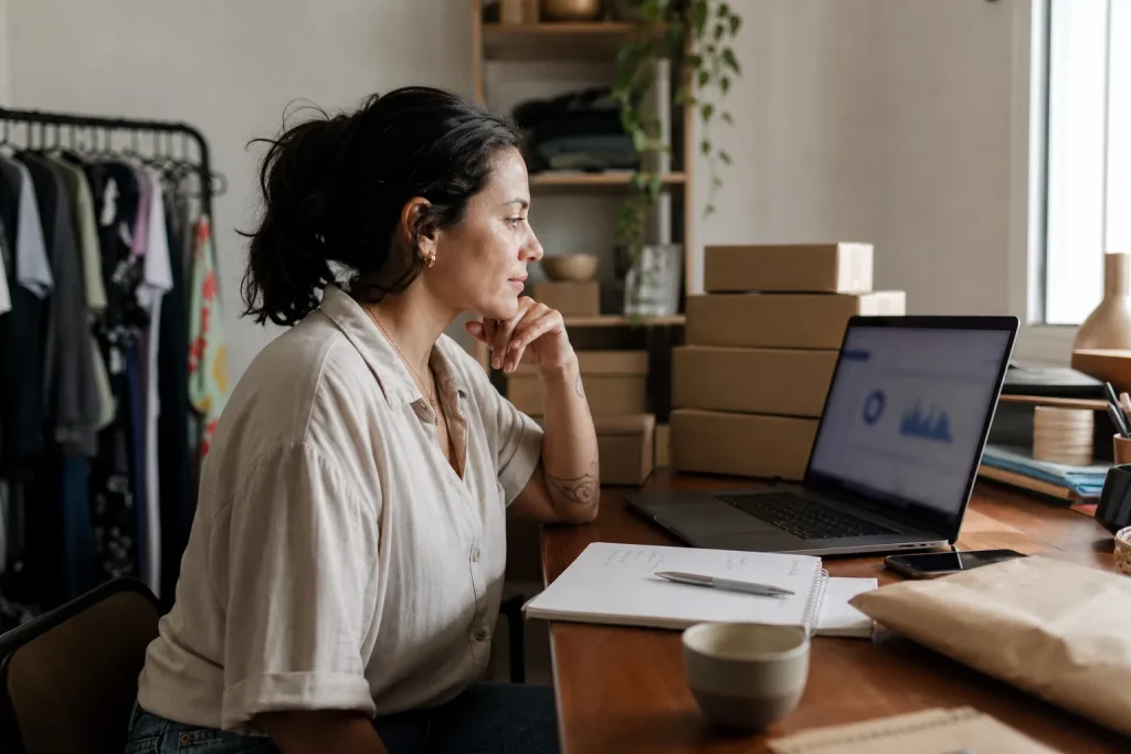 Lojista brasileira analisa painel de anúncios no notebook ao lado de caixas de produtos prontas para envio