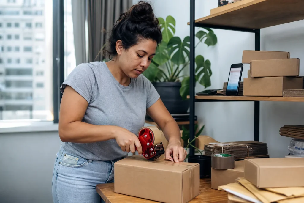 Mulher embala pedido de e-commerce em área improvisada dentro de apartamento