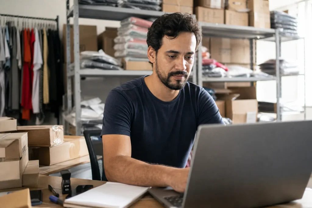 Dono de loja virtual brasileira conferindo pedidos em um notebook no estoque