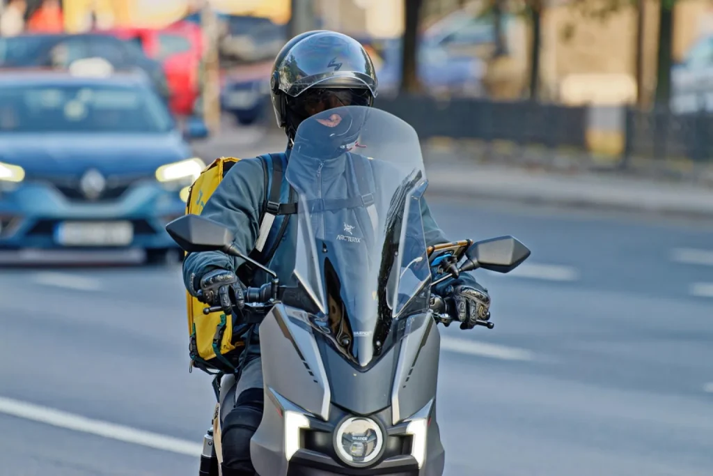 Entregador de moto recebe pacotes de uma funcionária de estoque em rua de São Paulo para entrega no mesmo dia