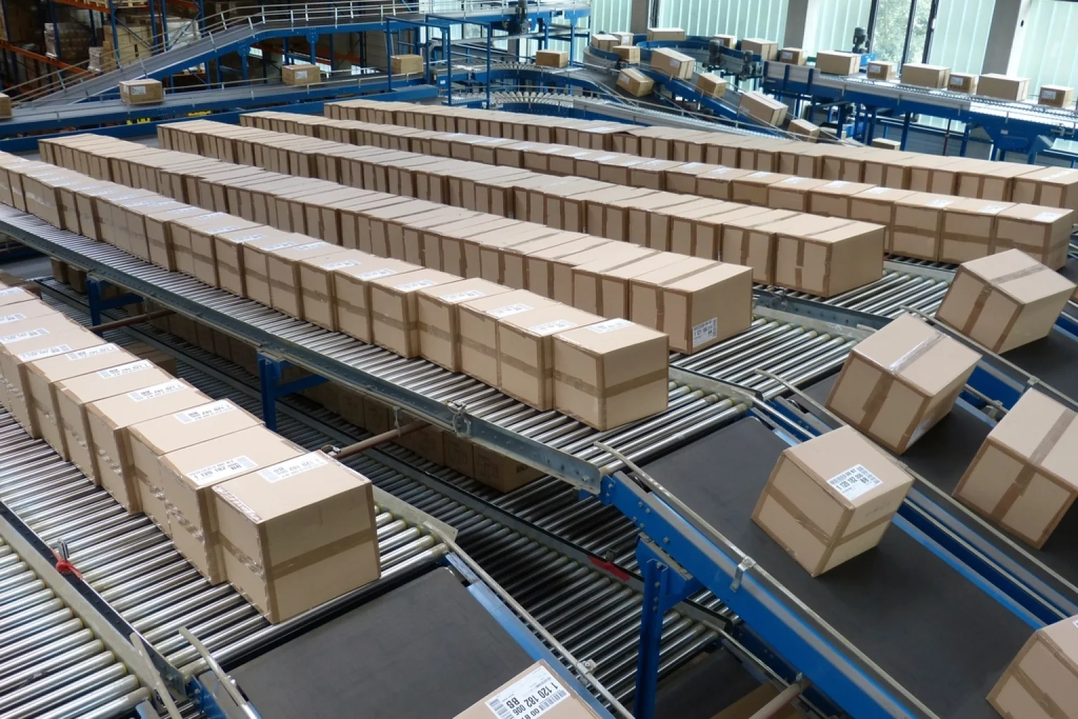 Funcionário confere caixa na esteira enquanto supervisora acompanha o prazo de expedição em um armazém de e-commerce